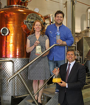 Heather Shade, co-owner of the Port Chilkoot   Distillery and President of the Distillers Guild of Alaska (holding a bottle of   their “50 Fathoms” gin); Jeremy Loyer, Managing Founder of Anchorage’s Bare   Distillery (holding a bottle of their “Truuli Peak” vodka); and Representative   Chris Tuck, D-Anchorage, and House Democratic Leader (holding a flask of orange   juice – just orange juice) celebrate the passage into law of House Bill 309 at a   press conference and reception at the Bare Distillery in Anchorage.  The new law   allows distilleries to serve local customers and tourists by giving facility   tours, offering tasting samples, and engaging in limited direct sales.